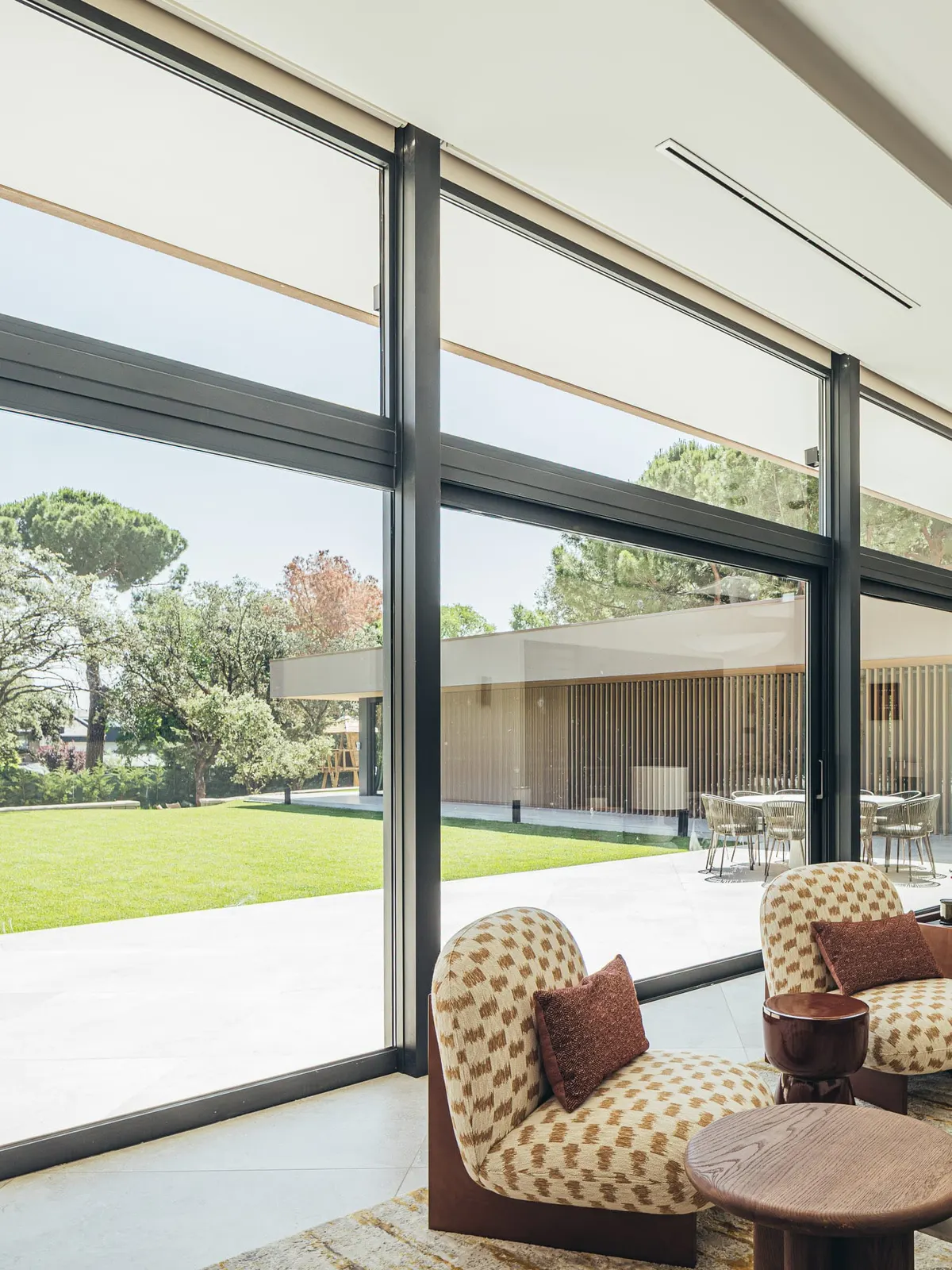 Salón de chalet en Boadilla con corredera panorámica de aluminio negro abierta al jardín